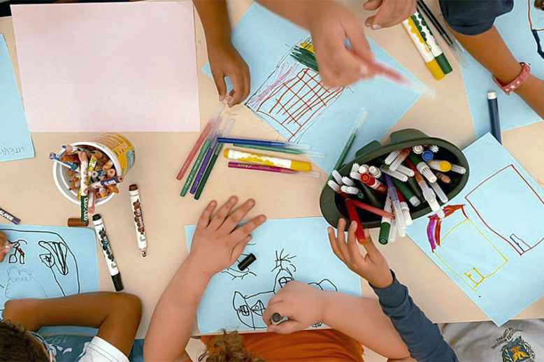 Várias crianças desenhando em uma mesa de escola